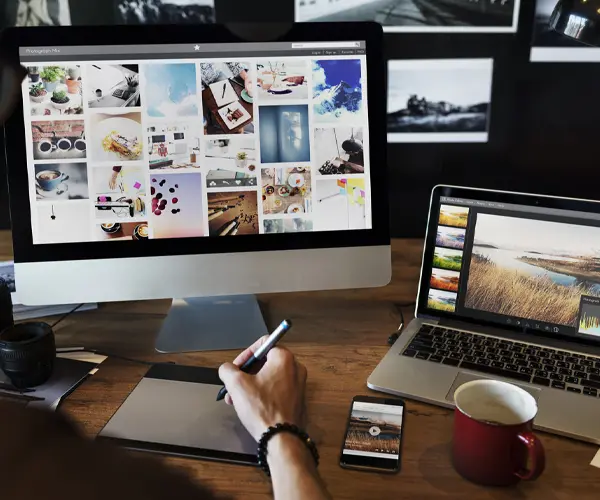 Individual focused on creative design and content production, using a laptop and tablet simultaneously.