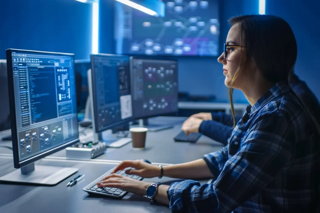 In a dark room, a woman is engaged with her computer, concentrating on IT governance and strategy work