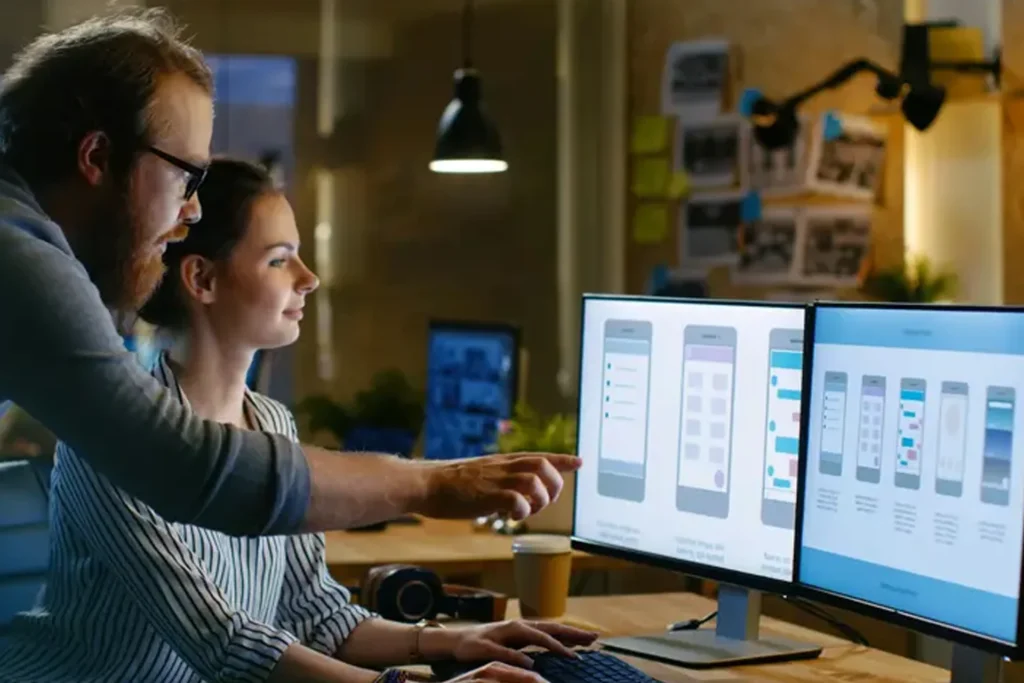 In an office, a man and woman work together on a computer, discussing user experience and mobile commerce solutions