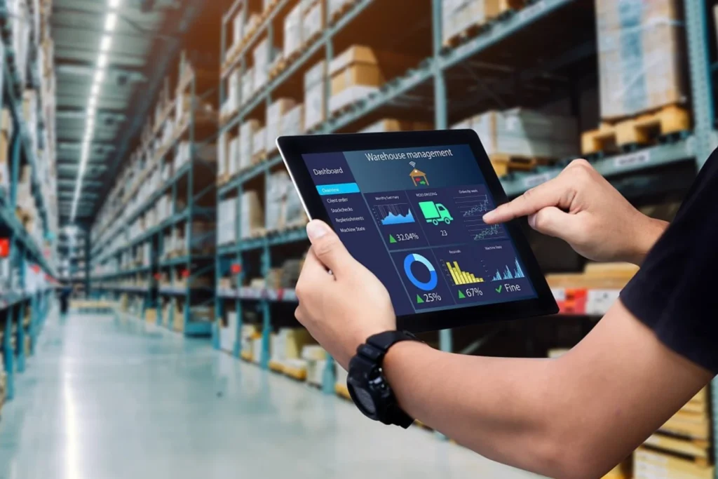 Man using a tablet in a warehouse filled with shelves stocked with various products, focusing on smart inventory management