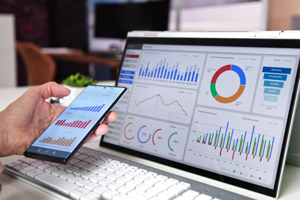 Person analyzes graphs on a laptop, using a smartphone for insights related to analytics and continuous optimization