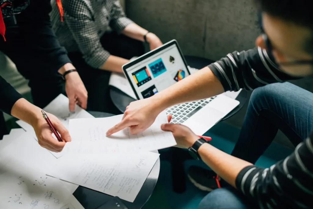 Three colleagues analyze papers and use laptops, discussing strategies for automating non-profit workflows