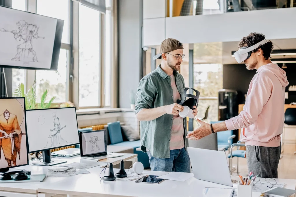 Two men in VR headsets engage with a computer, focused on developing games that captivate audiences