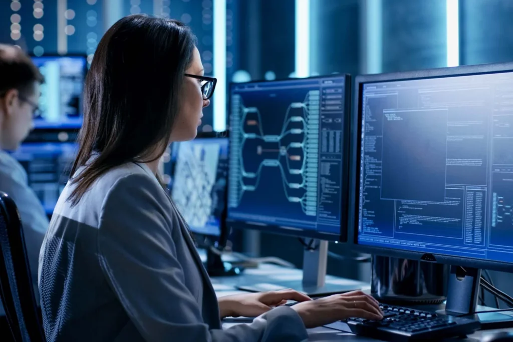 Woman in front of two monitors, actively working on cybersecurity management tasks on her computer