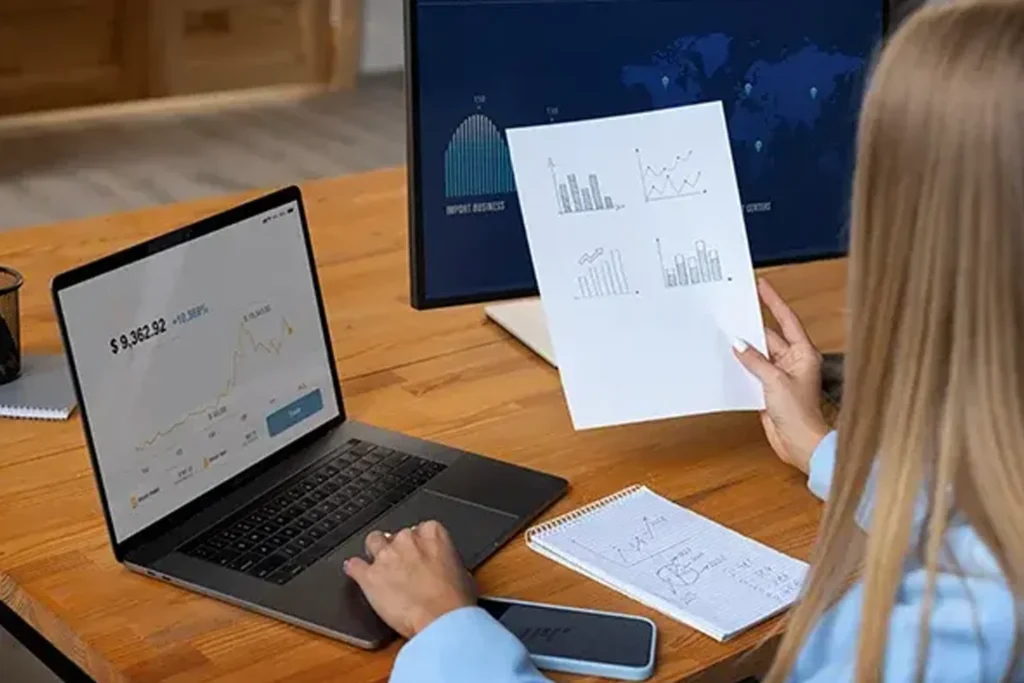 Woman working at a desk with two computers and a paper, concentrating on personalized logistics solutions