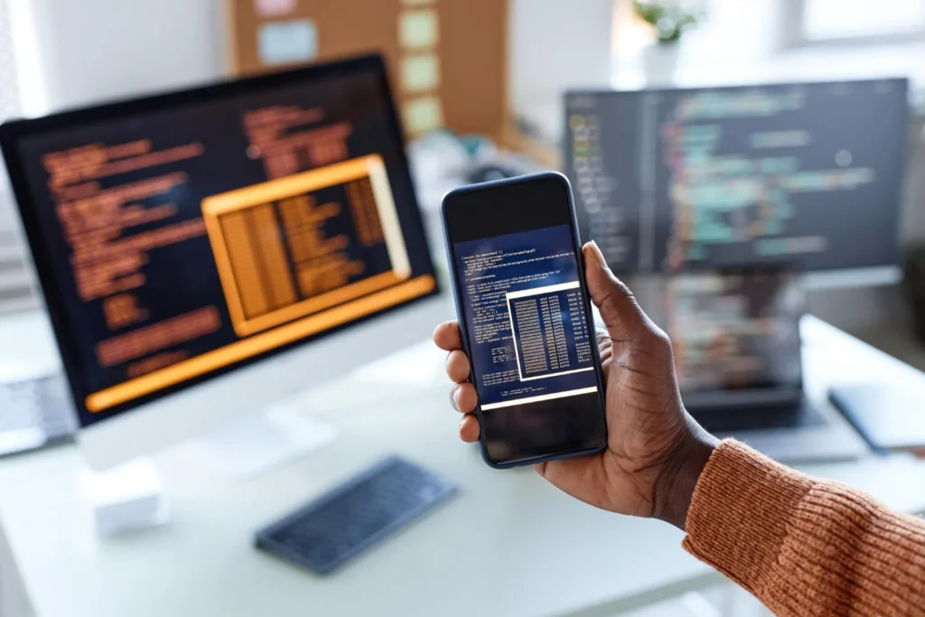A man with a smartphone stands in front of a computer screen showcasing industry-specific solutions
