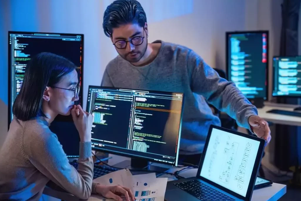 Two people engaged in remote IT support, working on computers with monitors in front of them