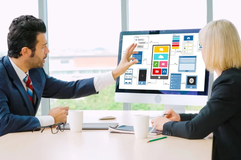 Two professionals in business attire examine a computer screen, exploring the advantages of custom web portal development